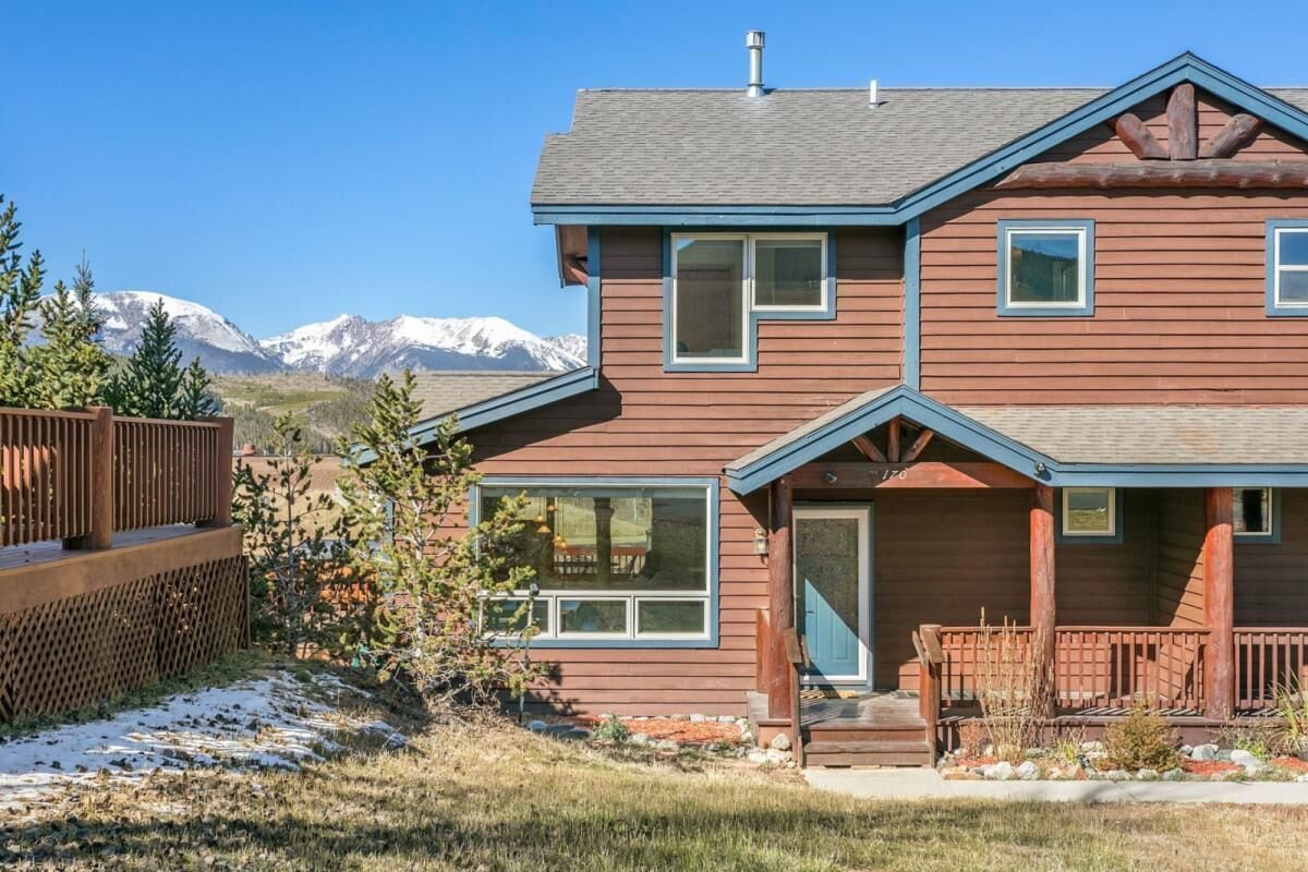A two-story house with a front porch, large windows, and a view of snow-capped mountains.