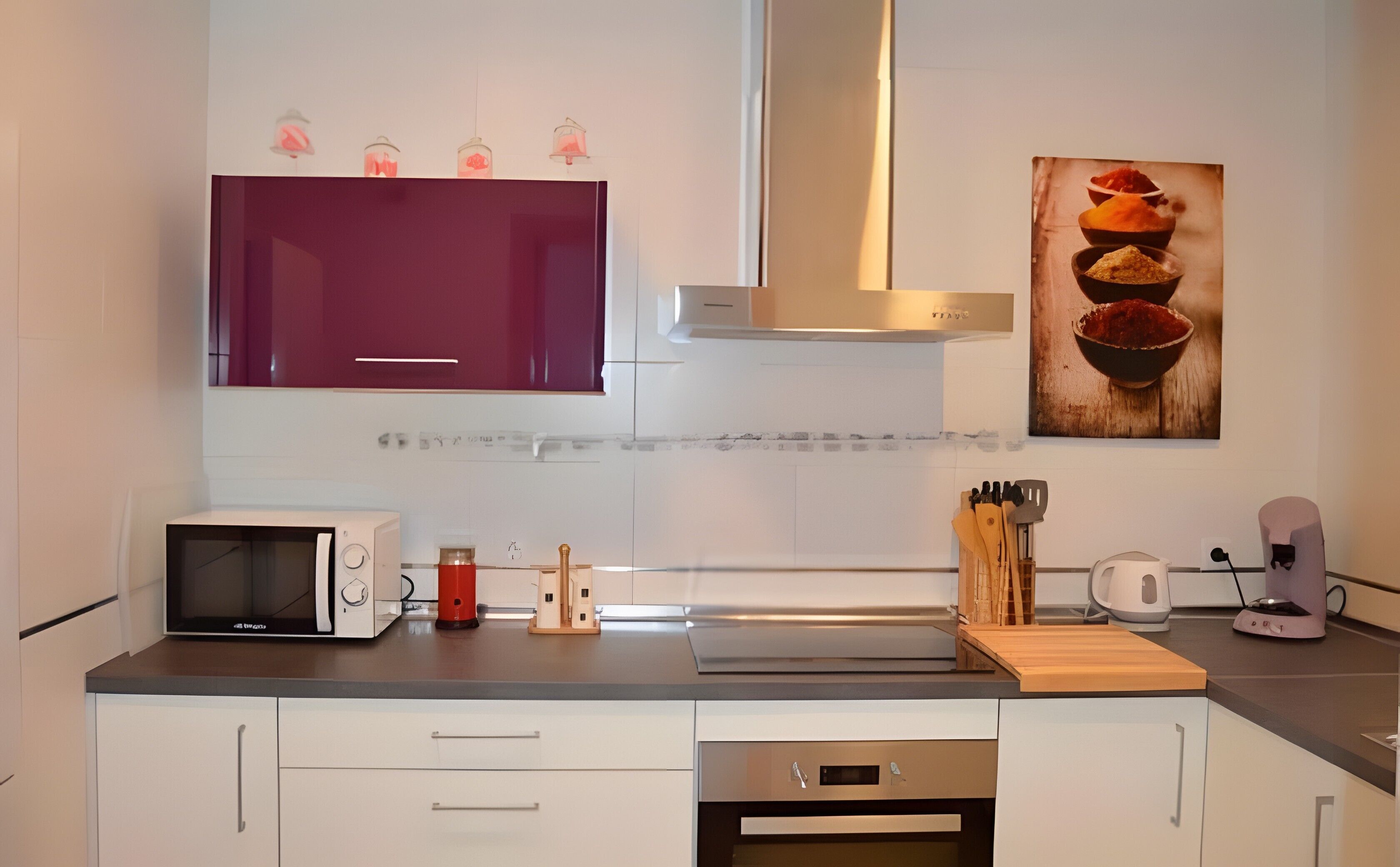 A modern kitchen with white cabinets, a microwave, a red kettle, and a coffee machine.
