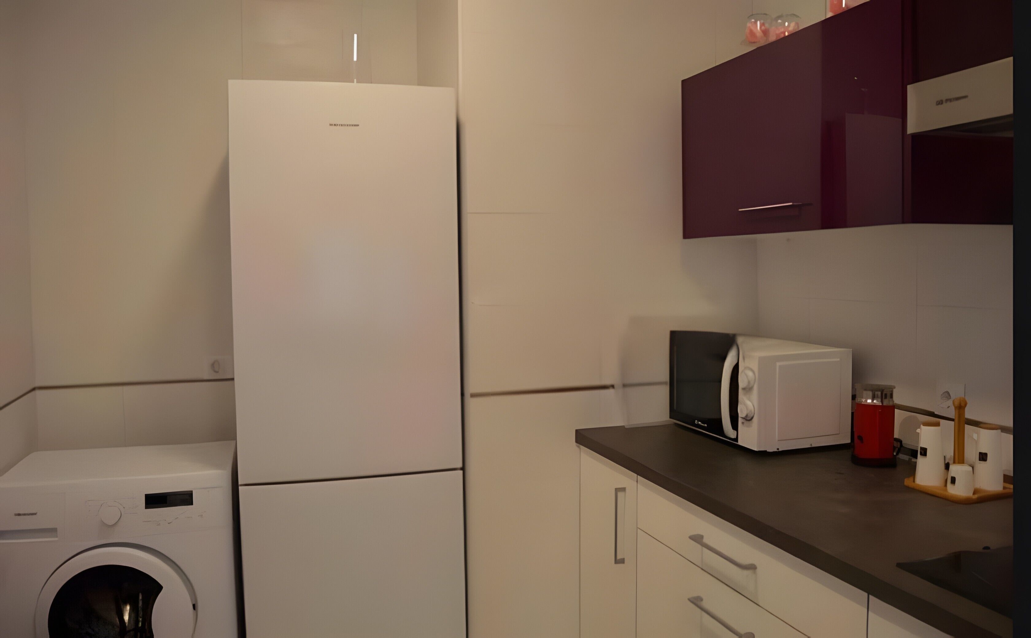 Una cocina compacta con lavadora, microondas y tostadora sobre la encimera.