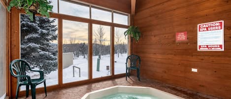 Une salle de spa dotée d’un bain à remous, de murs en bois et de grandes fenêtres donnant sur un paysage enneigé.