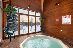 Une salle de spa dotée d’un bain à remous, de murs en bois et de grandes fenêtres donnant sur un paysage enneigé.