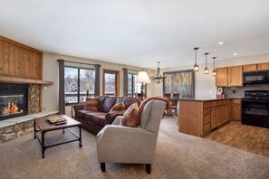 A spacious living room with a fireplace, a dining area, and a kitchen with wooden cabinets and a microwave. - Nature Retreat • Near Trails & Resorts • Hot Tub! (Silverthorne)