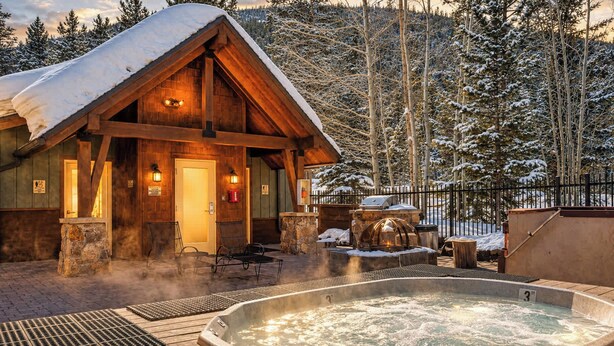 Eine Holzlodge mit Whirlpool und Sitzgelegenheit im Freien, umgeben von schneebedeckten Bäumen.