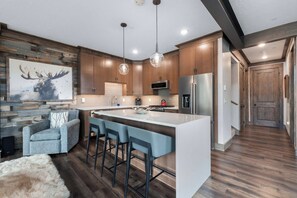 A modern kitchen with a central island, bar stools, a fireplace, and a large painting of a moose. - Alpine Ambiance | Luxury 4BR • 3 Decks • Hot Tub (Keystone)