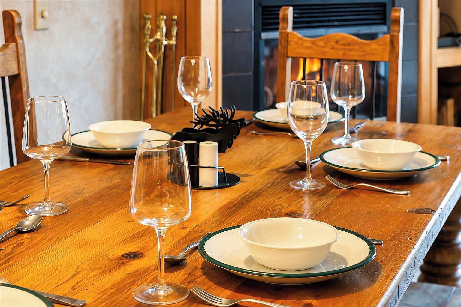 A wooden dining table set with white plates, clear wine glasses, and silverware.