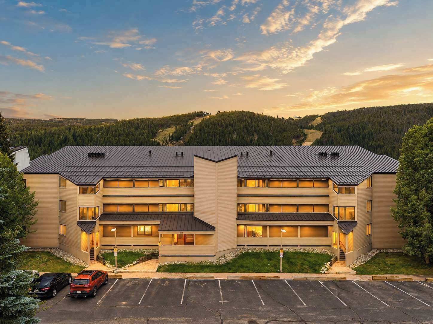 A multi-story hotel with a flat roof, a central entrance, and a parking lot.