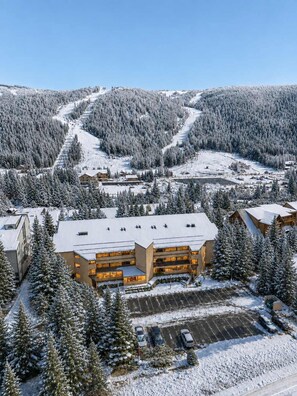 Un chalet à étages, un espace de stationnement et une piste de ski en arrière-plan.
