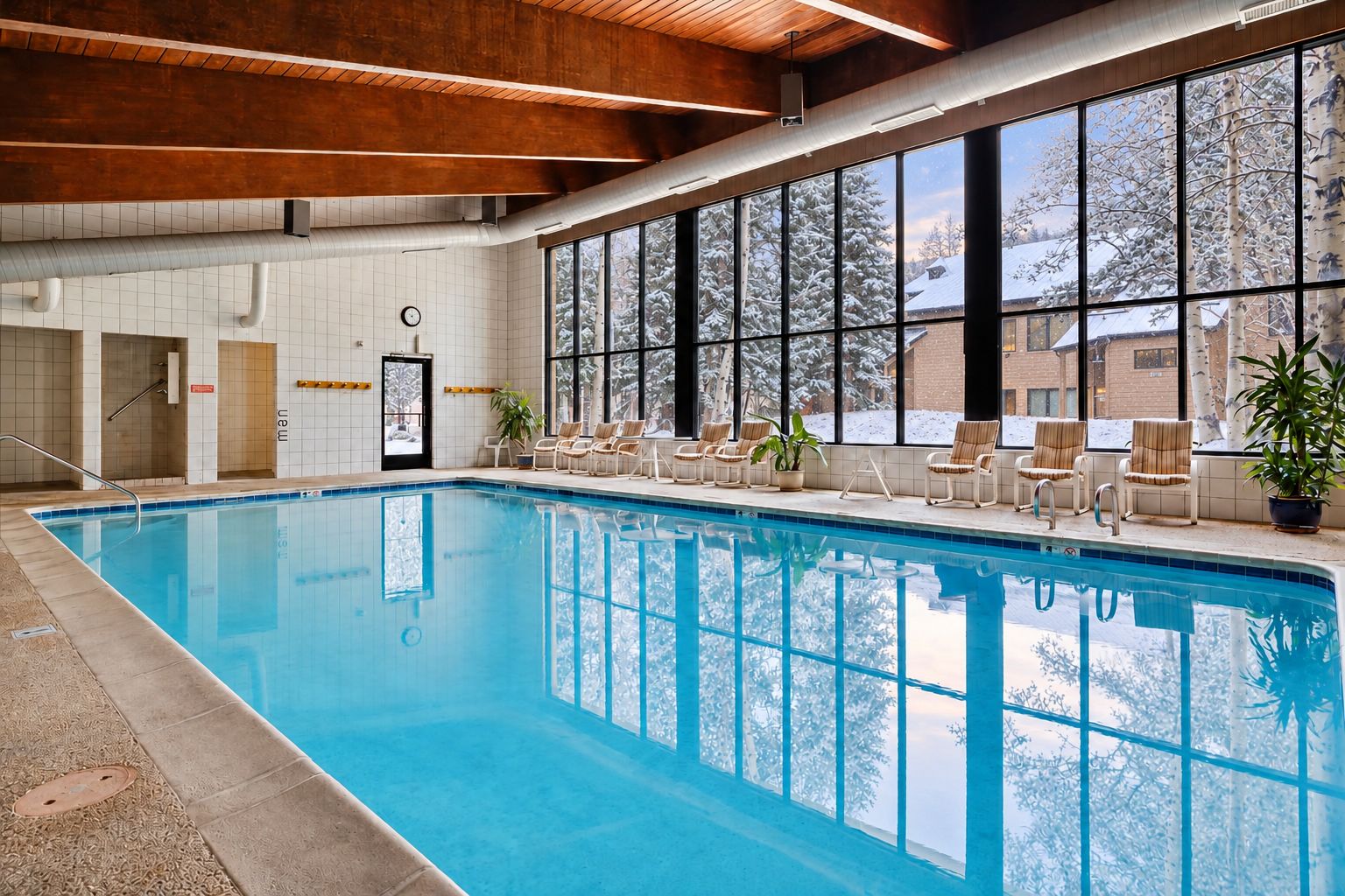 Une piscine intérieure offrant une vue dégagée sur les arbres enneigés à l’extérieur, grâce à de grandes fenêtres.