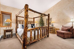 Ein Bett mit Baldachin im rustikalen Stil, ein Sofa, ein kleiner Tisch und ein Spiegel in einem Zimmer mit beigen Wänden.
