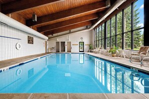 An indoor swimming pool with clear blue water, wooden ceiling beams, and large windows offering a view of trees. - Mountainside | Garage | Hot Tub | Steps to Lifts! (Keystone)
