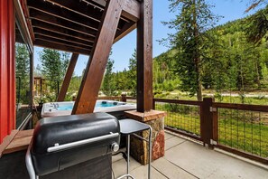 Ein überdachter Außenbereich mit Grill, Whirlpool und Blick auf eine bewaldete Landschaft.