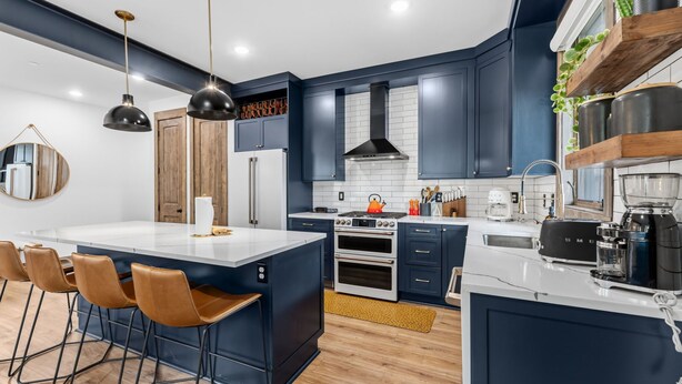 Una cucina moderna con mobili blu scuro, un'isola centrale con sgabelli da bar, elettrodomestici in acciaio inossidabile e luci a sospensione.