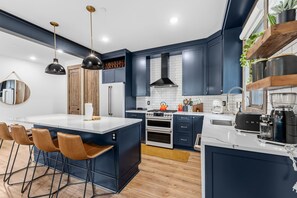 Una cocina moderna con armarios azul oscuro, una isla central con taburetes de bar, electrodomésticos de acero inoxidable e iluminación colgante.