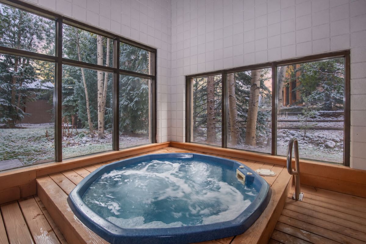 Un bain à remous avec une terrasse en bois, de grandes fenêtres et une vue sur les arbres.