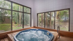 A hot tub in a room with large windows, wooden flooring, and a view of trees. - Slopeside | Hot Tub • Garage • Pool • Ski Locker! (Keystone)