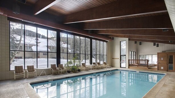 An indoor swimming pool with clear windows, lounge chairs, and a wooden ceiling. - Slopeside | Hot Tub • Garage • Pool • Ski Locker! (Keystone)