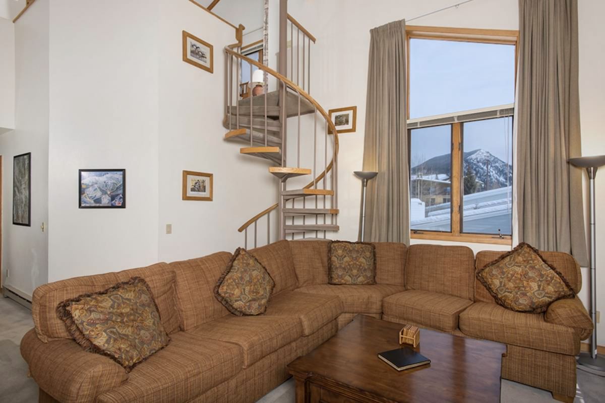 A living room with a large sectional sofa, a wooden coffee table, a spiral staircase, and framed pictures on the walls.