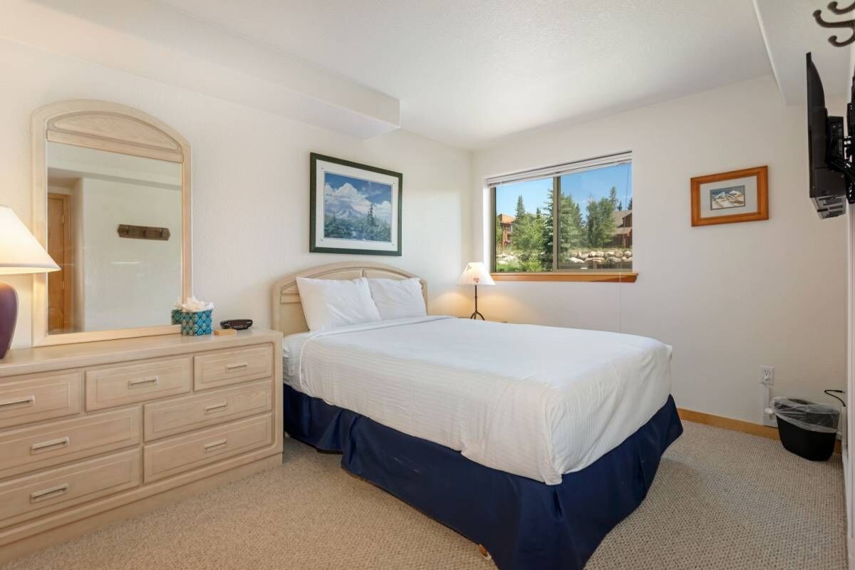A bedroom with a bed, dresser, mirror, window, and framed picture.