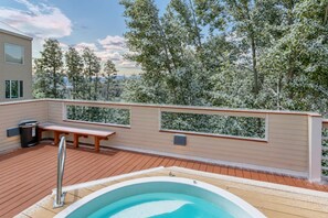 Eine Dachterrasse mit Whirlpool, Holzliegen und Blick auf verschneite Bäume.