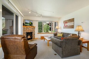 A living room with a stone fireplace, leather armchair, grey sofa, and a television. - Watch Hill Hideaway | Hot Tub • Near Six Resorts! (Silverthorne)