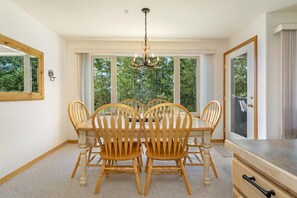 A dining room with a round table and six wooden chairs, large windows with curtains, and a chandelier. - Watch Hill Hideaway | Hot Tub • Near Six Resorts! (Silverthorne)