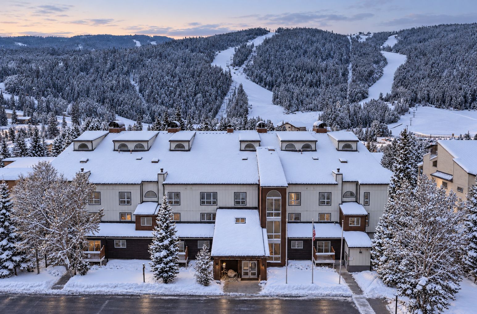 A multi-story hotel with a symmetrical facade, snow-covered surroundings, and a ski slope in the background.