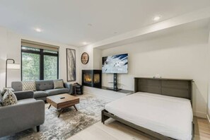 A modern bedroom with a bed, a sofa, a fireplace, and a TV. - New Riverfront Home | Near Six Resorts • Hot Tub! (Silverthorne)