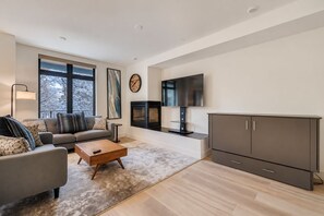 A modern living room with a sofa, coffee table, TV, fireplace, and cabinets. - New Riverfront Home | Near Six Resorts • Hot Tub! (Silverthorne)