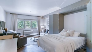 Ein modernes Hotelzimmer mit Bett, Schreibtisch, Stuhl und Fenster mit Blick auf Bäume.