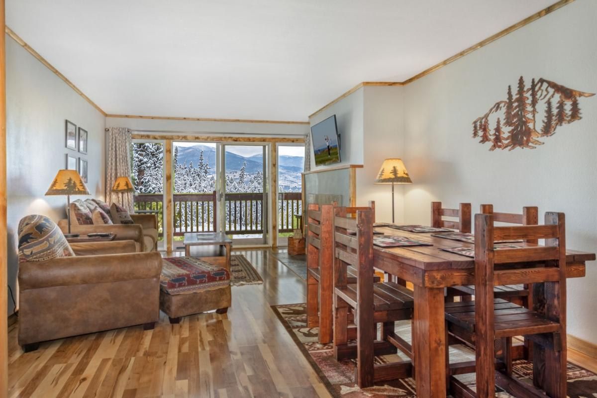 A living room with a wooden floor, a sofa, a dining table with chairs, and a TV on the wall.