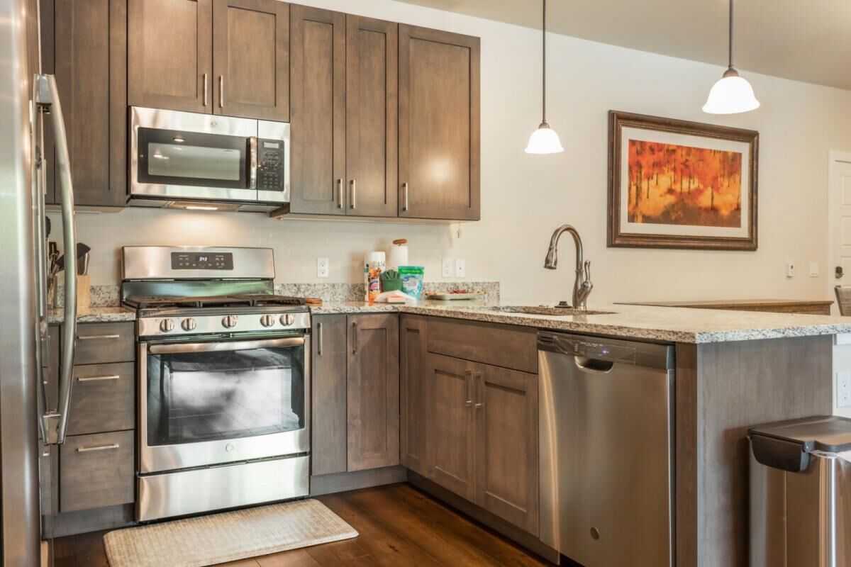 A modern kitchen with stainless steel appliances, wooden cabinets, and a granite countertop.