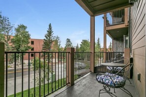 A balcony with a table and chairs, a view of a street and trees, and a building with a balcony. - The Sail Loft • Ideal Location • Near Six Resorts! (Dillon)