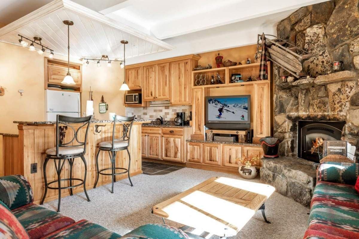 A kitchen with wooden cabinets, a stone fireplace, a TV, and a bar area with stools.