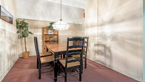 Et spiseområde med et træbord og stole, en hængende lampe, en potteplante og en vægmonteret hylde.