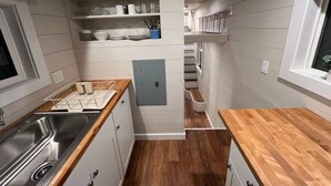 Una cucina compatta con un lavello in acciaio inossidabile, un piano di lavoro in legno, mobili bianchi e una colonna a giorno.
