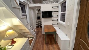 Una cucina compatta e moderna, con elettrodomestici integrati, un tavolo da pranzo in legno e un televisore fissato alla parete.