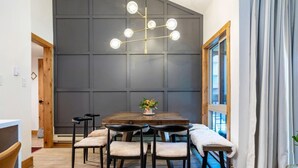 A dining area with a wooden table, six chairs, a chandelier, and a large window with curtains. - The Wild Irishman | Hot Tub • Free Shuttle • Pool (Dillon)