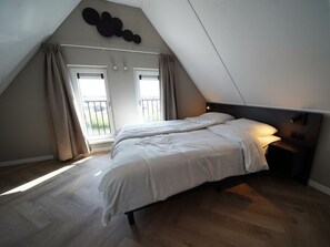 A bedroom with a sloped ceiling, a bed with white bedding, a bedside table with a lamp, and a view of the outdoors through a window. - Holiday Home in Kampen With Terrace (Kampen)