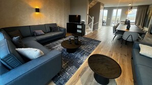 Uma sala de estar moderna com sofá, mesa de centro e televisão. Escada leva a uma varanda.