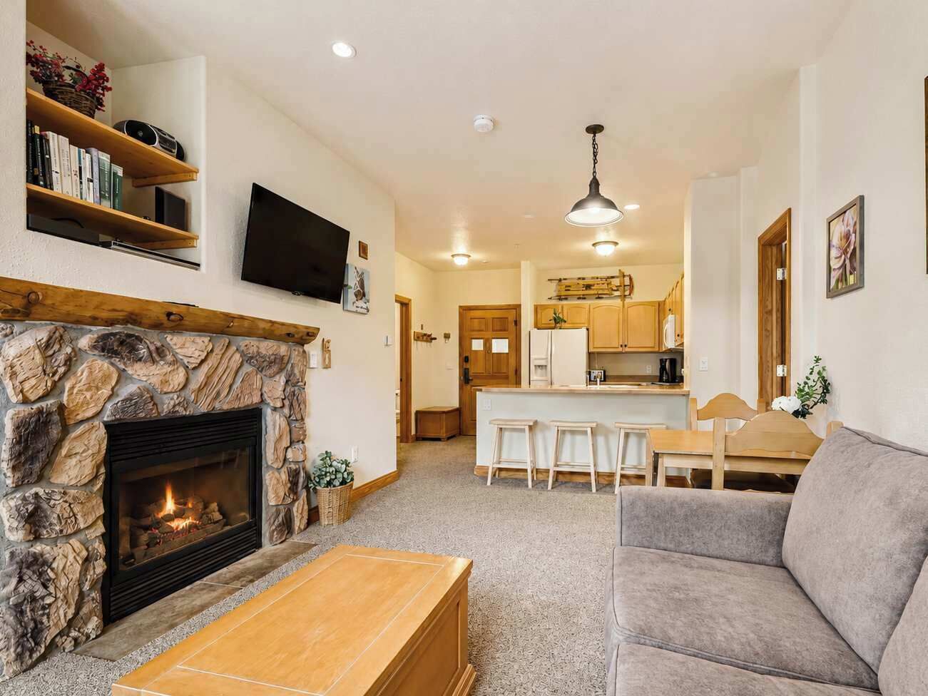 A living room with a stone fireplace, a flat-screen TV, and a grey sofa.