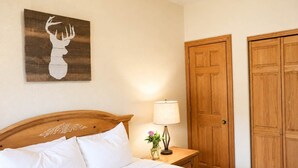 Un dormitorio con cabecera de madera, lámpara de noche, cuadro de cabeza de ciervo enmarco y puerta doble.