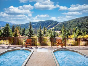 Ein Poolbereich mit zwei Whirlpools, einer Holzterrasse und Blick auf einen bewaldeten Gebirgszug.