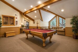 A pool table in a room with a high ceiling, wooden beams, a sofa, and a window with a view of trees. - Slopeside | Hot Tub | Garage | Walk to Lifts! (Keystone)