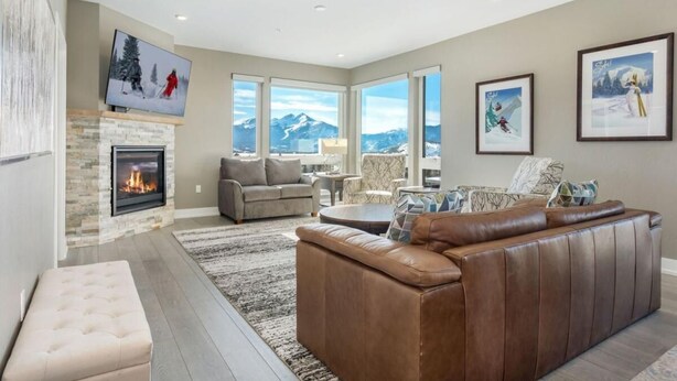 A modern living room with a fireplace, leather sofa, and large windows offering mountain views. - Penthouse Retreat • Stunning Views • Near Resorts! (Dillon)
