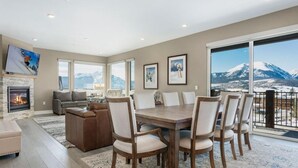 A spacious living room with a fireplace, a dining area with a large table and chairs, and a balcony with a mountain view. - Penthouse Retreat • Stunning Views • Near Resorts! (Dillon)