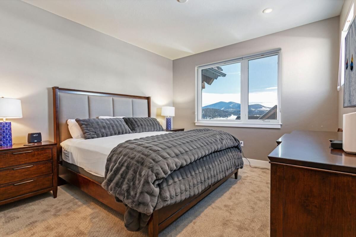 A bedroom with a bed, nightstands, a dresser, and a window with a mountain view.