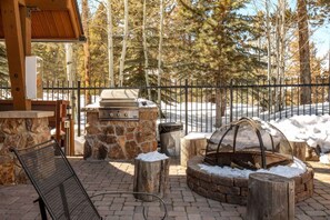 An outdoor patio with a stone barbecue, a fire pit, and a metal chair. - Keystone Retreat | Minutes from Mountain • Hot Tub (Keystone)