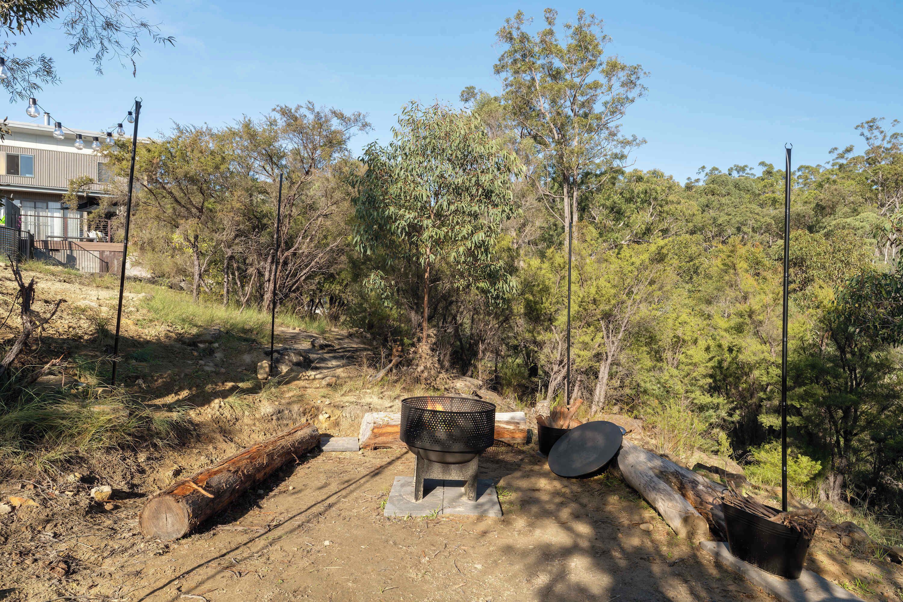 A campsite with a fire pit, surrounded by trees and a building in the background.
