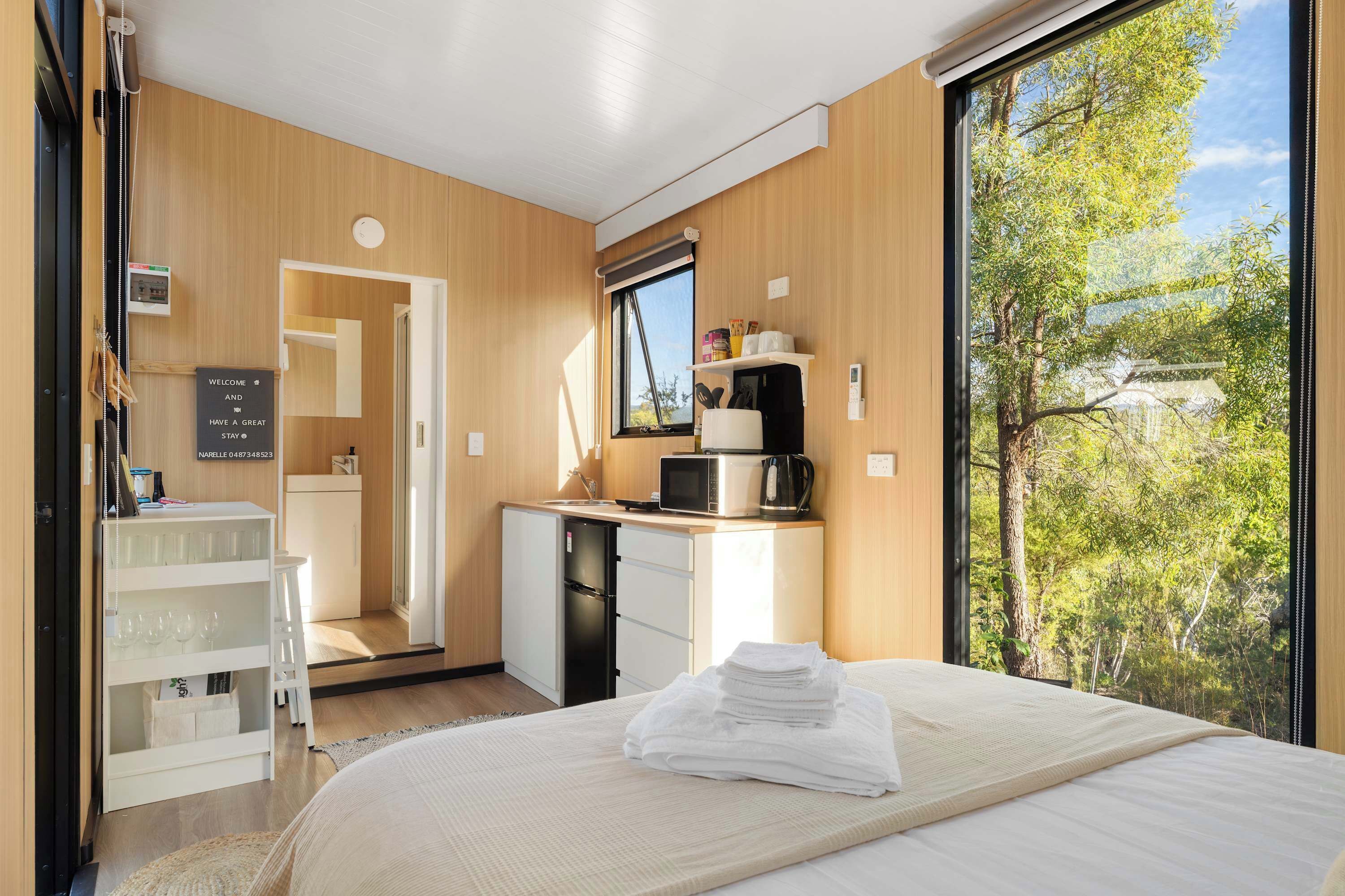 Een moderne hotelkamer met een bed, een bureau met een computer, een magnetron en uitzicht op bomen.