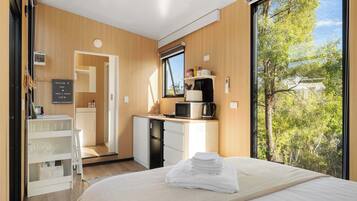 Een moderne hotelkamer met een bed, een bureau met een computer, een magnetron en uitzicht op bomen.